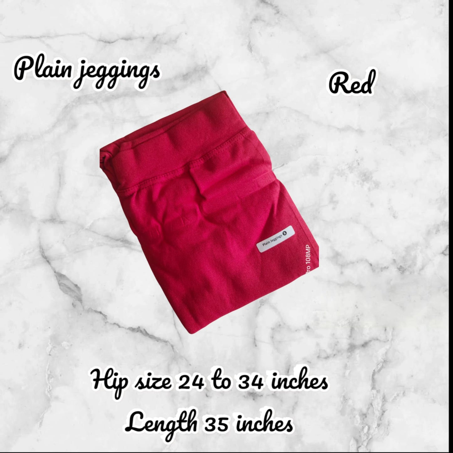 Folded red jeggings on a marble surface with text indicating size and length.